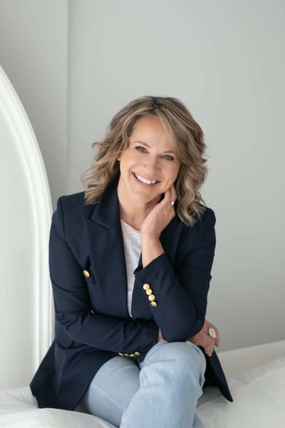 Lisa smiling with her chin resting on her hand, wearing a navy blazer and a white t-shirt.